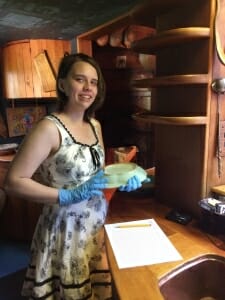 Young woman standing by kitchen shelves wearing nitrile gloves and holding a ceramic dish.