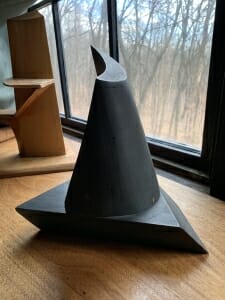 small wood model painted black which has triangular base and a twisting cone on top, getting narrower as it goes up.