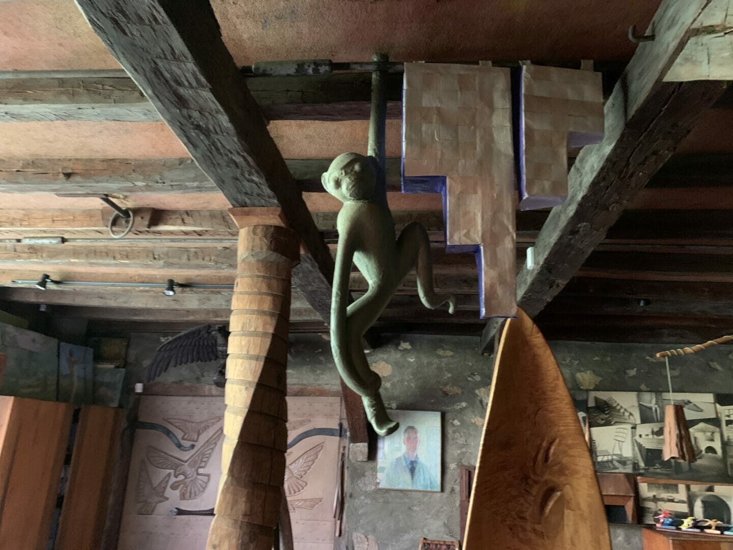 ceramic sculpture of monkey hangs by one arm, to the right are two stepped paper forms painted blue on the sides