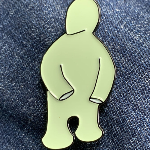 small enamel pin of a cartoonish light green figure on a denim background.